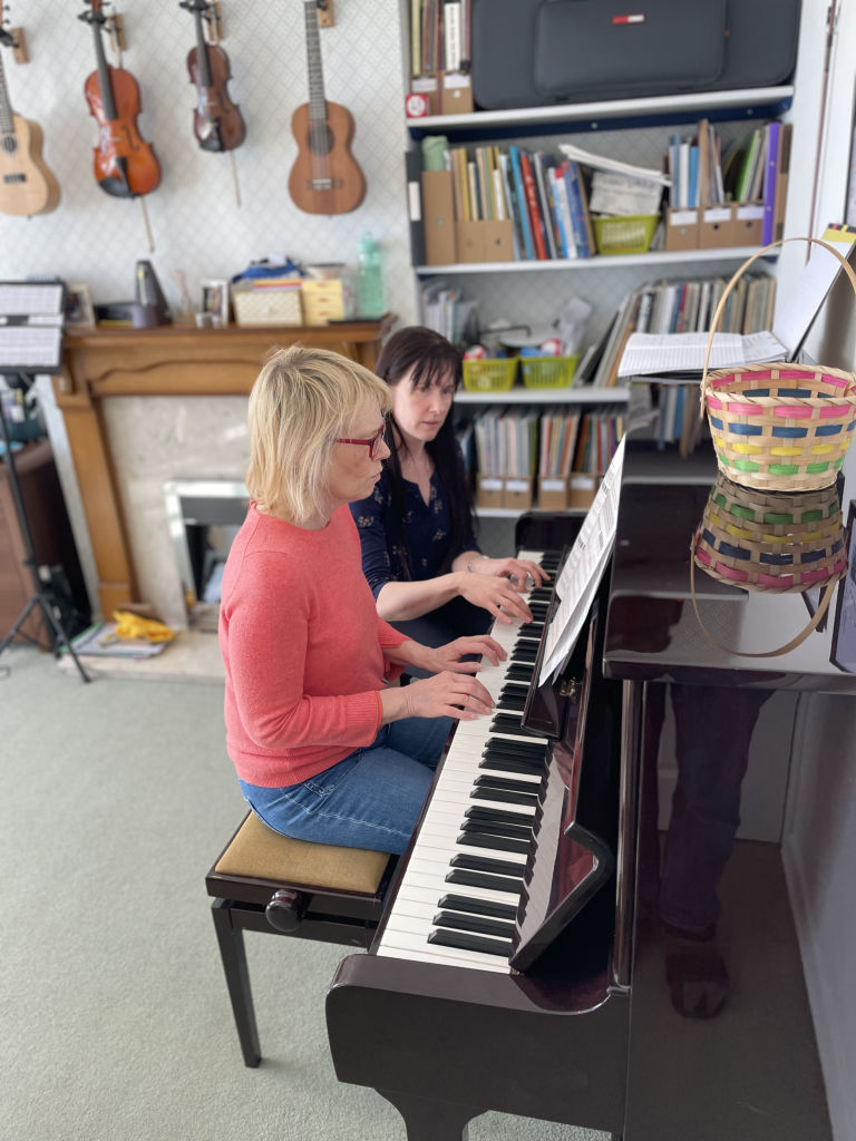 Rosie plays the piano alongside her student.