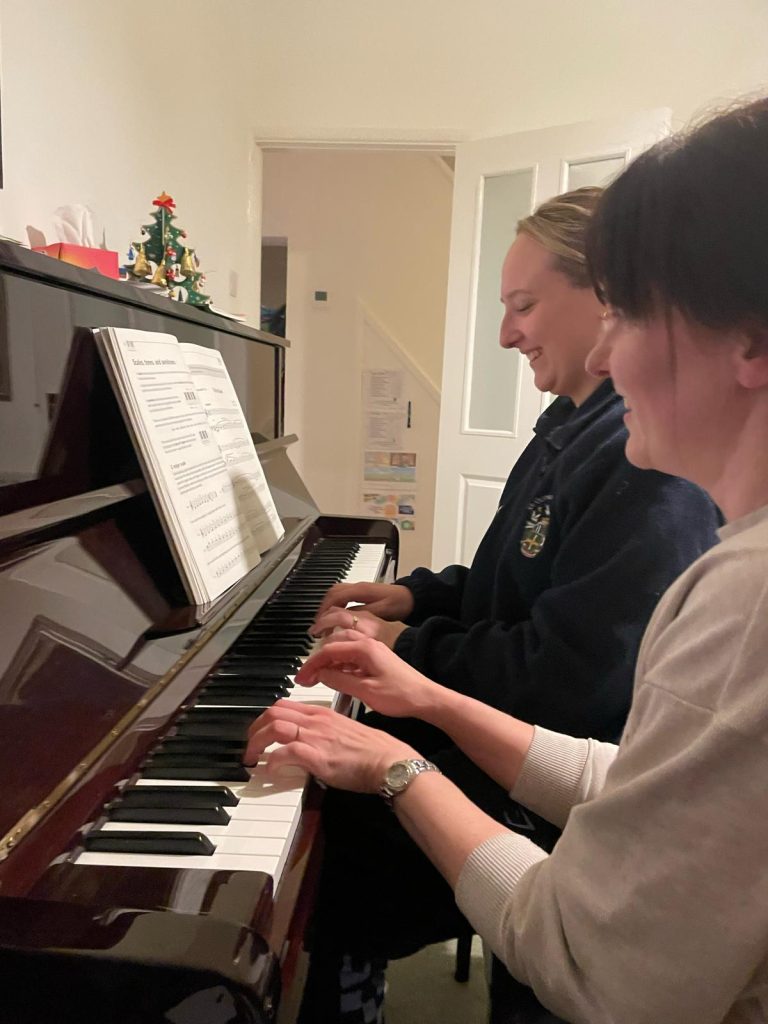 Rosie and her student sit at a piano, playing together.