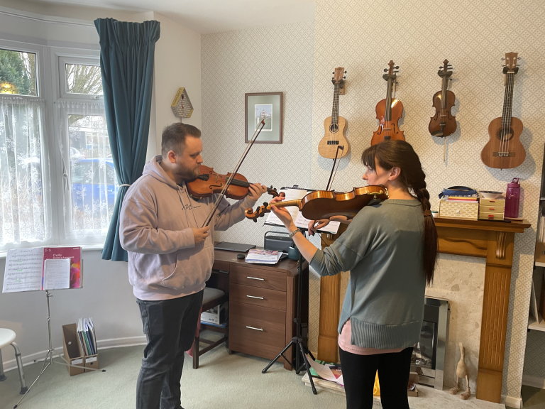 Rosie and her student stand opposite each other, playing their violins.