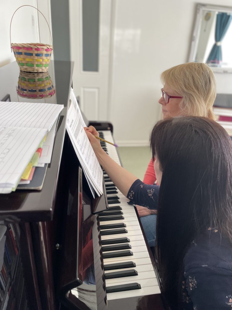 Rosie and her student sit at a piano, studying the sheet music